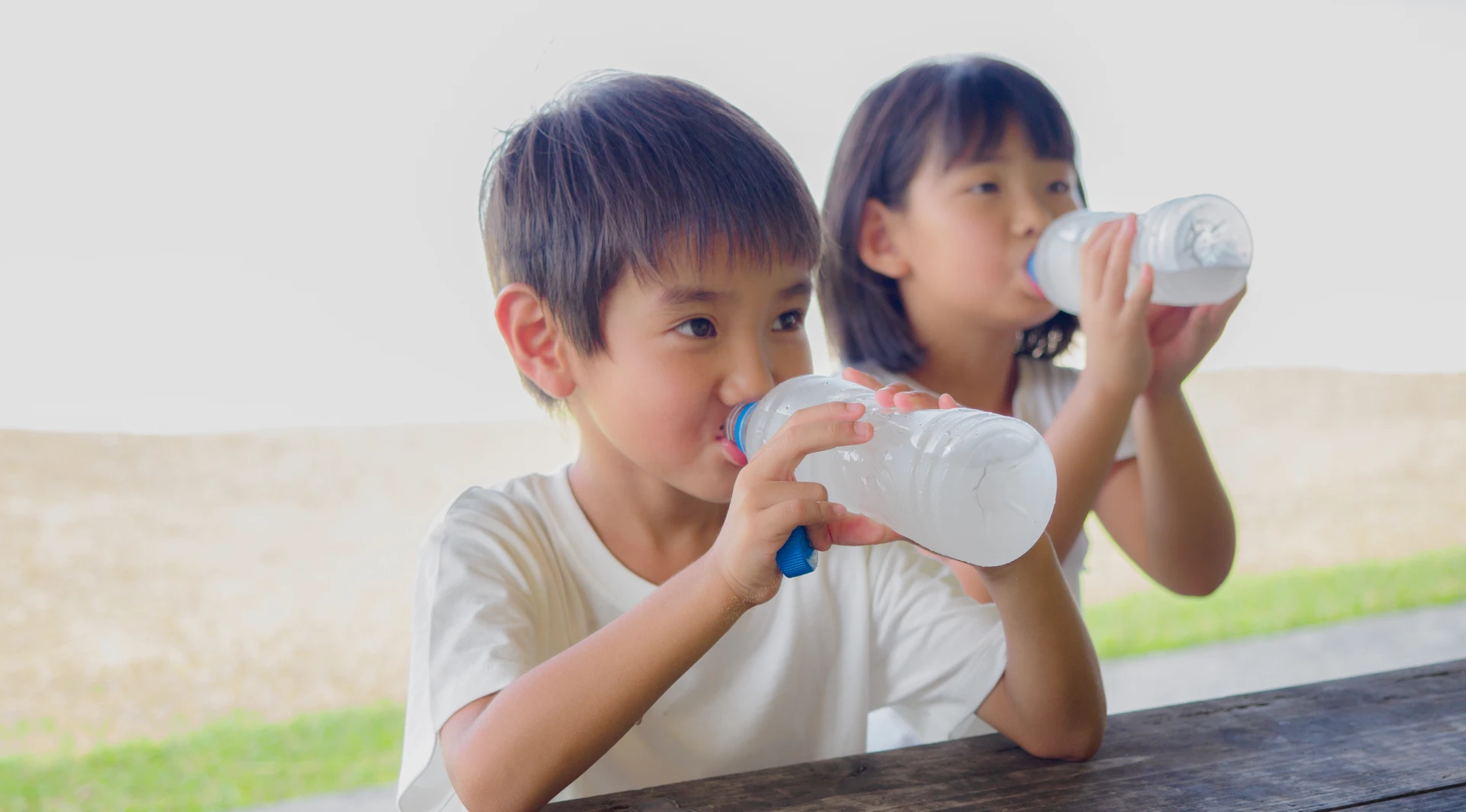Young siblings enjoying bottled water outside.