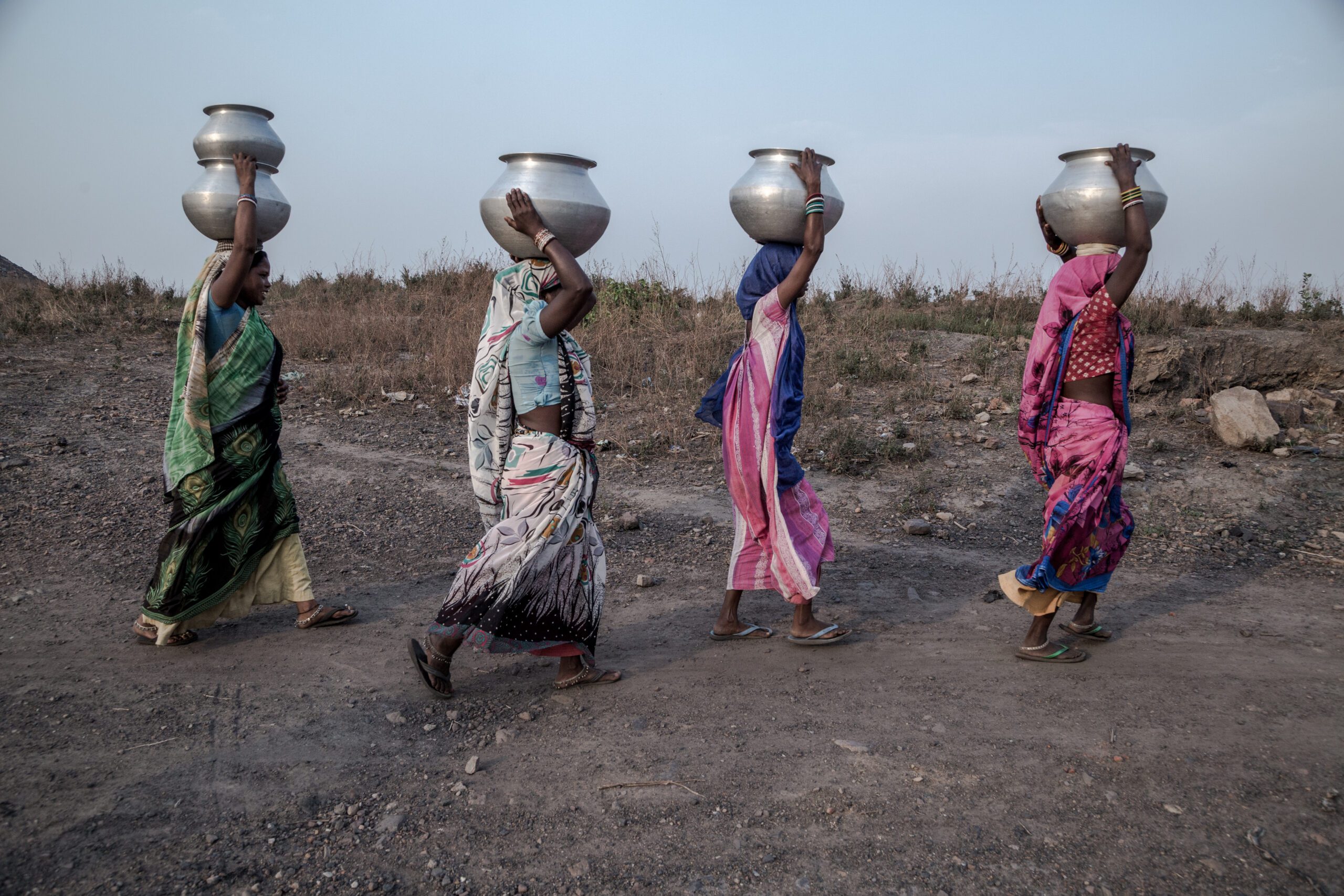 Four women walking with metal pots